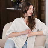 Modal sitting on white sofa in a living room wearing Chunky Knit Women's Waffle Cardigan in Oat over blue jeans
