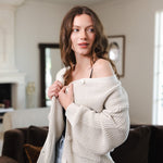 Modal standing in a living room wearing Chunky Knit Women's Waffle Cardigan in Oat over black camisole and blue jeans
::: Model is 5'8" wearing size XS ///
