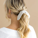 Woman with blonde hair styled in a ponytail with a oat scrunchie against a beige background