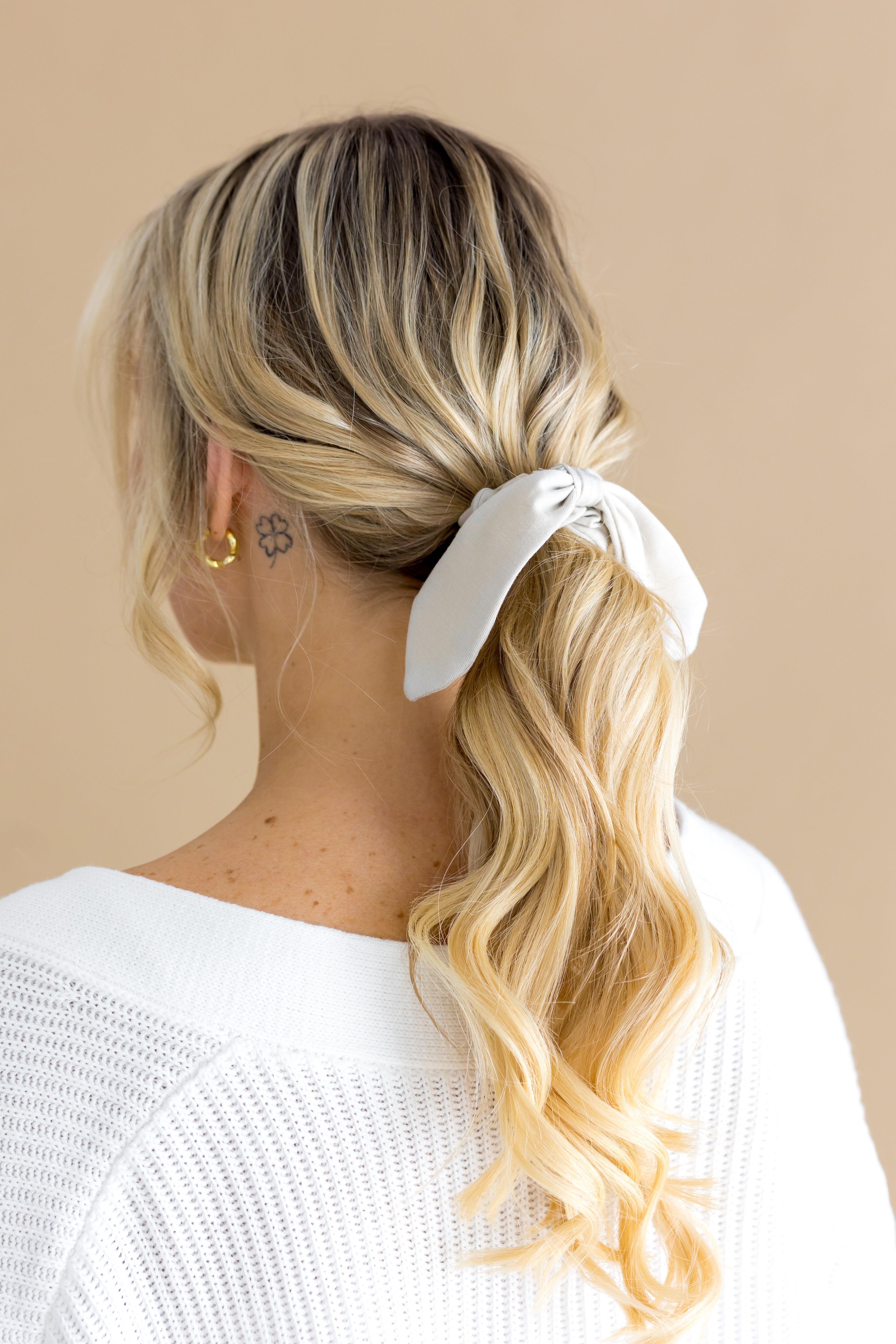 Woman with blonde hair styled in a ponytail with a oat scrunchie against a beige background