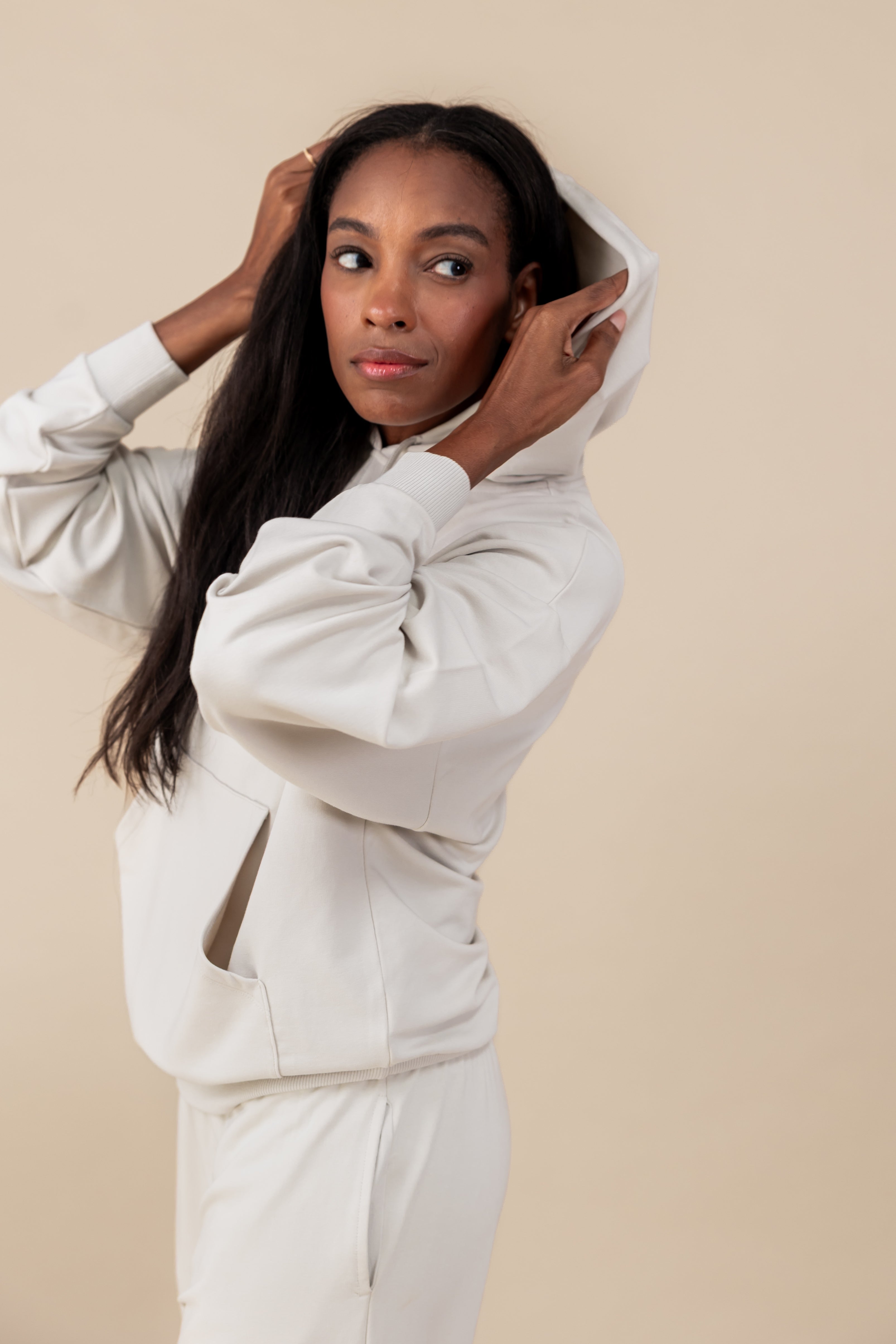 Side pose of Modal wearing Women's Hoodie in Oat color over similar color jogger pants on a beige background