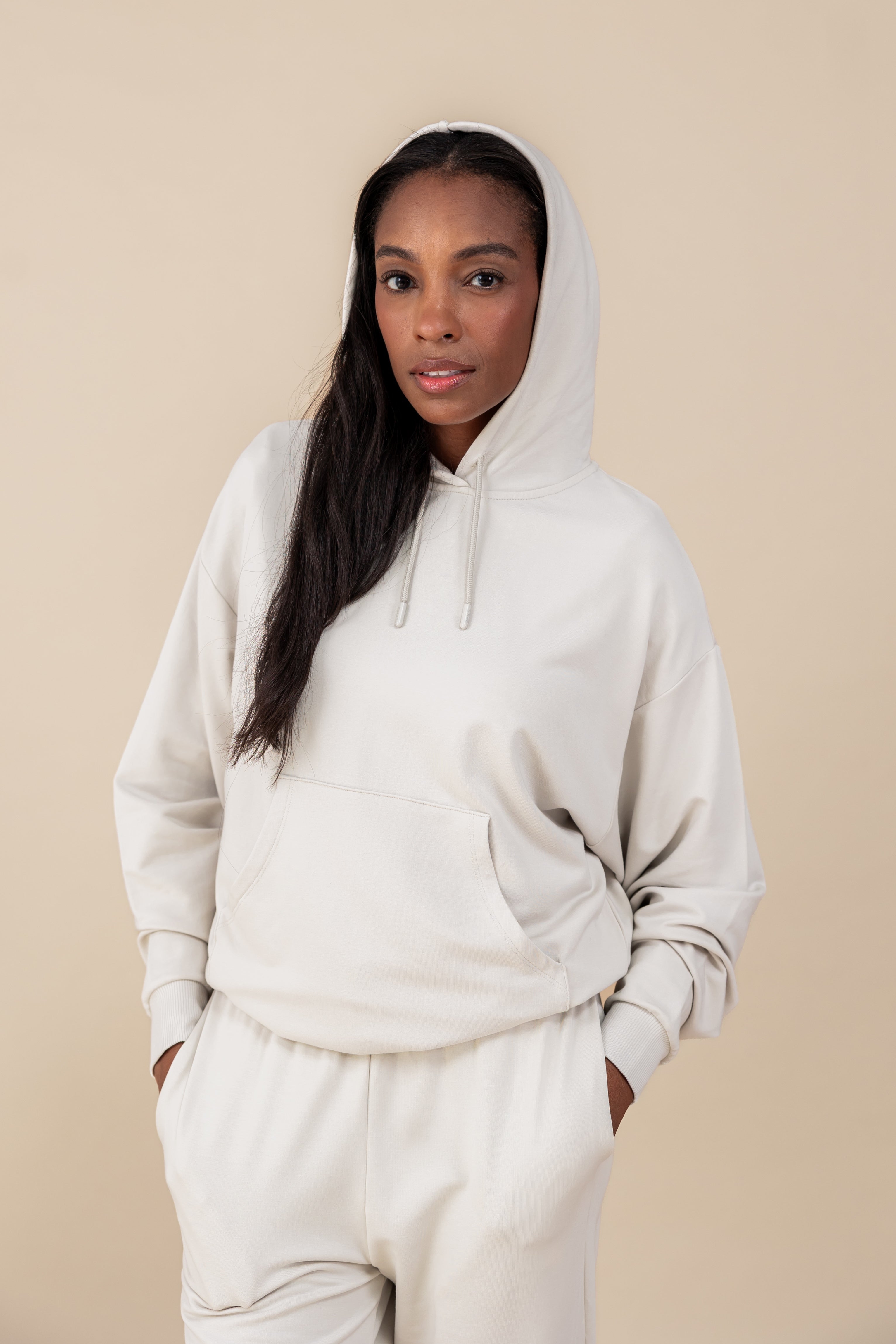 Modal wearing Women's Hoodie in Oat color over similar color jogger pants on a beige background
::: Model is 5'9" wearing size M ///