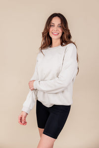 Woman smiling pulling up one arm sleeve wearing a sweatshirt in oat and biker shorts in black