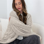Woman sitting on a white couch snuggling in a oversized beige knitted cardigan.