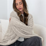 Woman sitting on a white couch snuggling in a oversized beige knitted cardigan.
