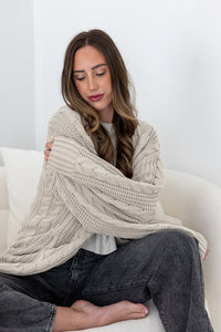 Woman sitting on a white couch snuggling in a oversized beige knitted cardigan.