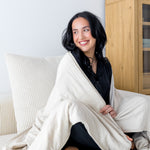 Woman cozy with a cream colored throw blanket around shoulders