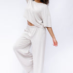 Female model standing with her eyes closed with one leg up and bent and one hand on top of her head wearing the Women's Short Sleeve Tee in Oat and matching wide leg pants