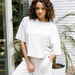 Woman standing in front of a white brick wall while modeling the Kyte Women's Short Sleeve Tee in Oat