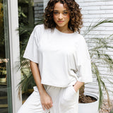 Woman standing in front of a white brick wall while modeling the Kyte Women's Short Sleeve Tee in Oat