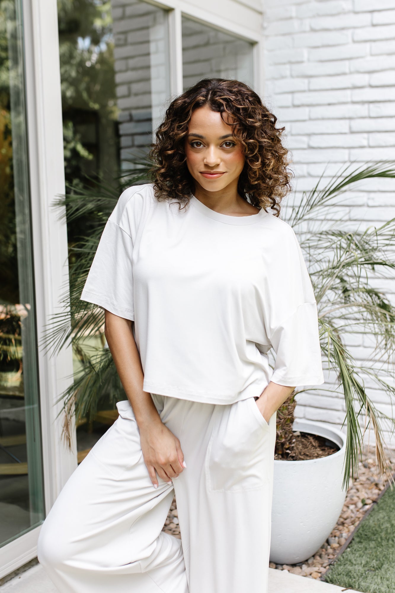 Woman standing in front of a white brick wall while modeling the Kyte Women's Short Sleeve Tee in Oat