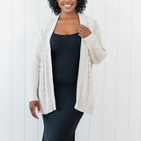 Model wearing the Chunky Cable Knit Cardigan in Oat layered over the Ribbed Cami dress in Midnight