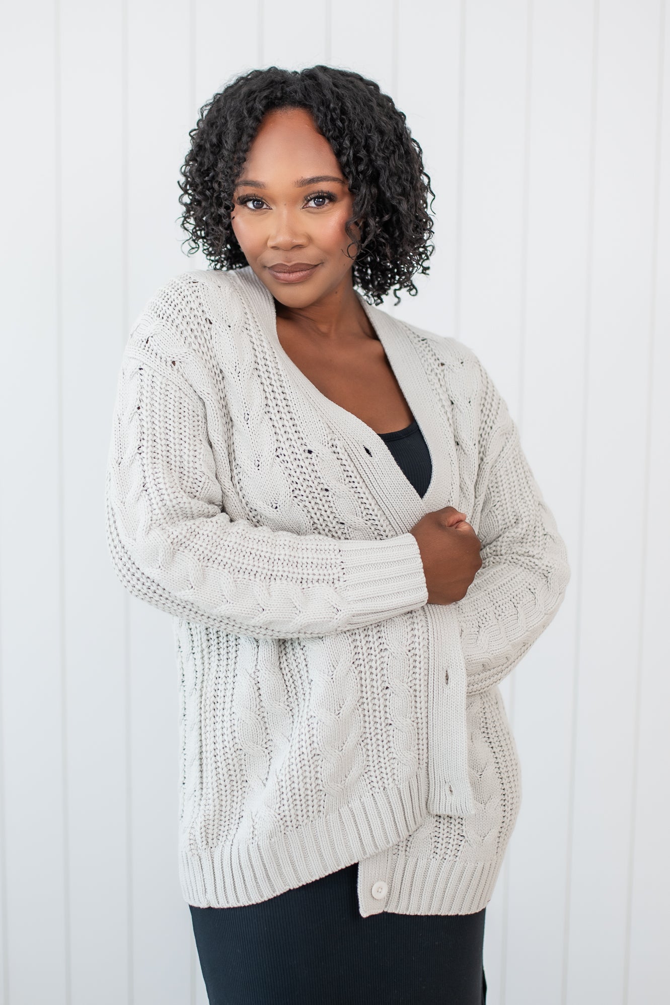 Model curled up in Chunky Cable Knit Cardigan in Oat