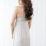 Woman wearing a light gray dress against a white wooden panel background showing the back of the dress