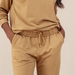 Modal wearing Women's Jogger Pants in Ochre color with pockets under similar color women's sweatshirt on a beige background