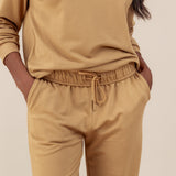 Modal wearing Women's Jogger Pants in Ochre color with pockets under similar color women's sweatshirt on a beige background