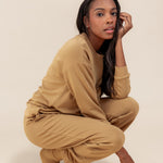 Modal posing in Women's Jogger Pants in Ochre color under similar color women's sweatshirt on a beige background