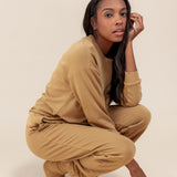 Modal posing in Women's Jogger Pants in Ochre color under similar color women's sweatshirt on a beige background