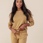 Woman wearing Women's Sweatshirt in Ochre color over similar color jogger pants on a beige background