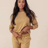 Woman wearing Women's Sweatshirt in Ochre color over similar color jogger pants on a beige background