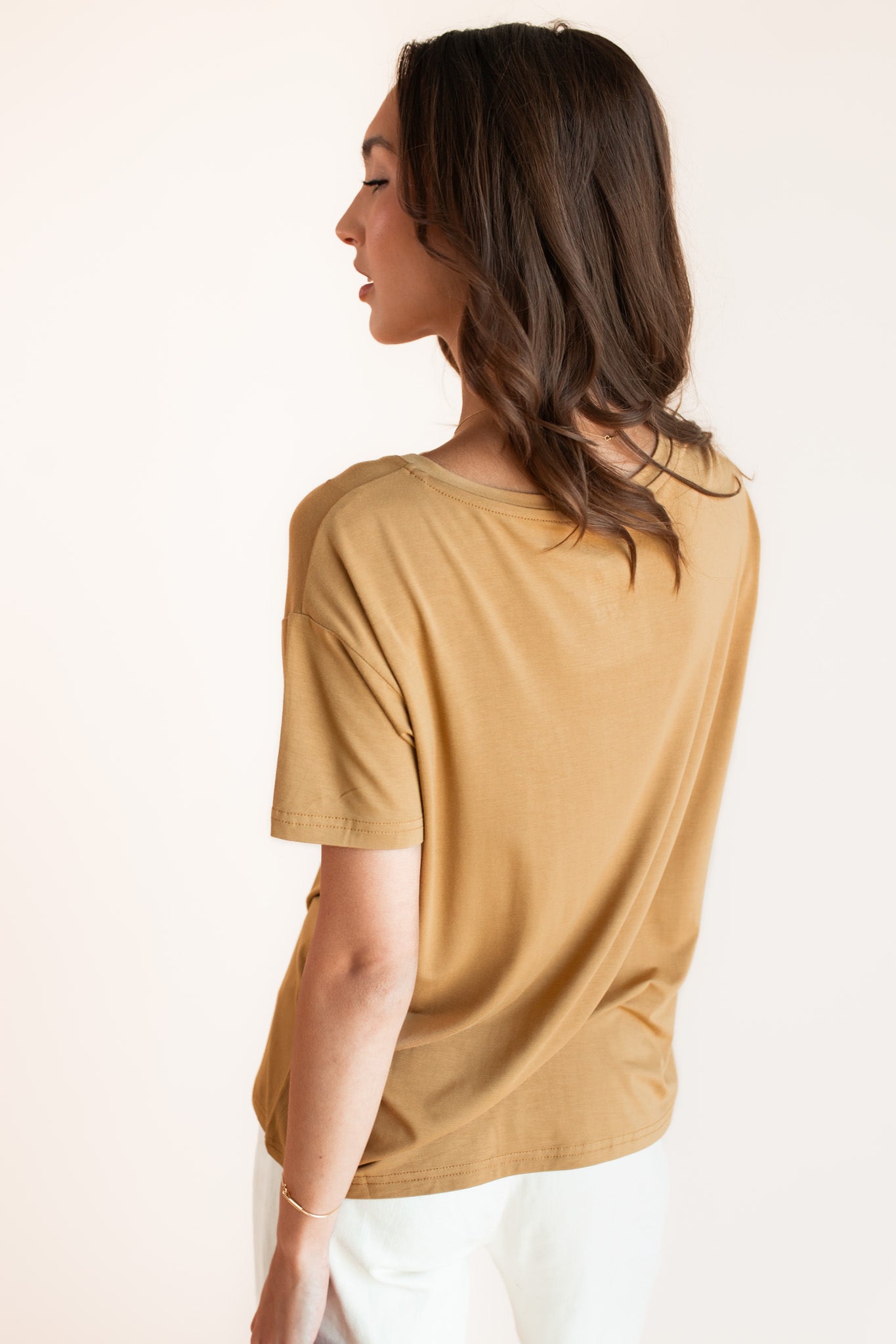 Woman modeling a mustard yellow v-neck oversized tee, showing back