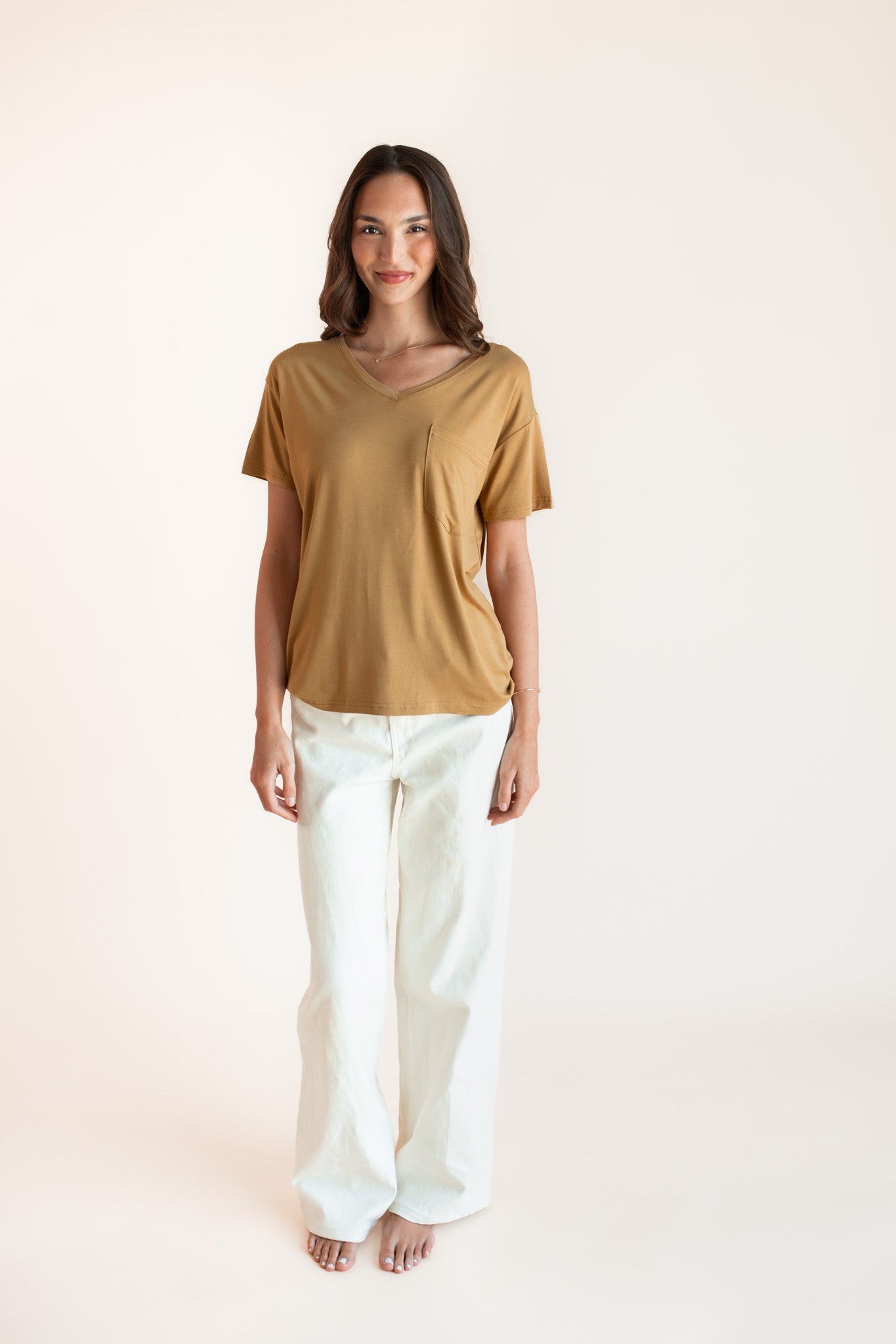 Woman modeling a mustard yellow v-neck oversized tee with white jeans