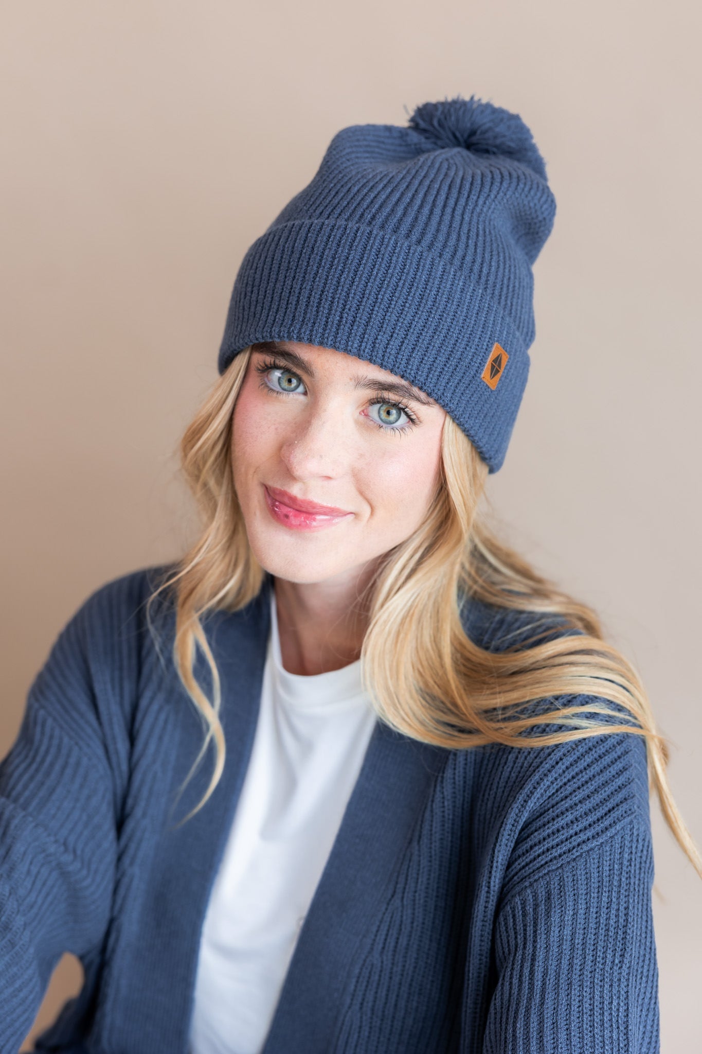 Modal wearing Chunky Knit Adult Pom beanie in Oxford over white t-shirt and chunky knit women's cardigan in oxford on a beige background