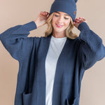 Modal wearing Chunky Knit Adult Pom beanie in Oxford over white t-shirt and chunky knit oversized cardigan in oxford on a beige background