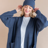 Modal wearing Chunky Knit Adult Pom beanie in Oxford over white t-shirt and chunky knit oversized cardigan in oxford on a beige background