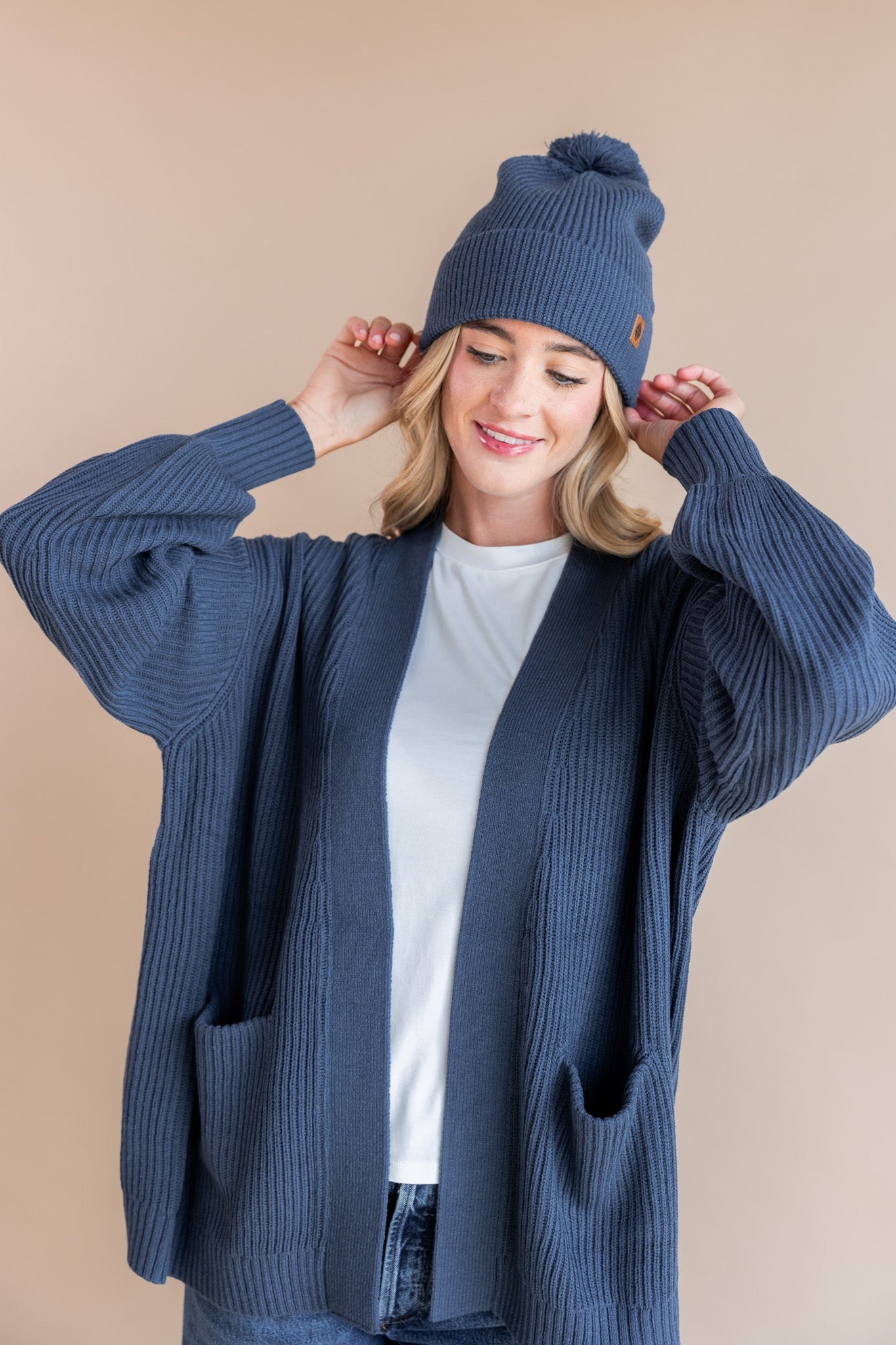 Modal wearing Chunky Knit Adult Pom beanie in Oxford over white t-shirt and chunky knit oversized cardigan in oxford on a beige background