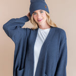 Modal wearing Chunky Knit Adult Pom Beanie in Oxford over white t-shirt and chunky knit oversized cardigan in oxford on a beige background