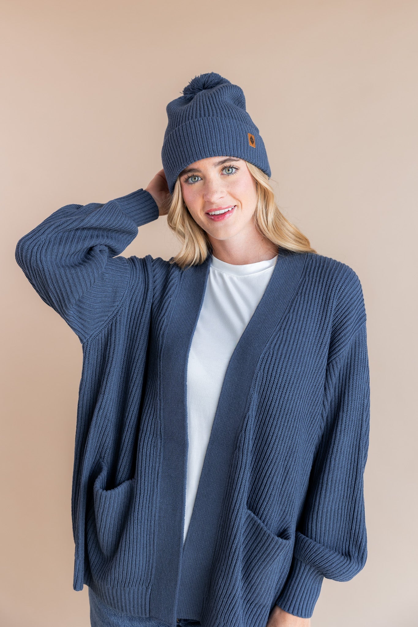 Modal wearing Chunky Knit Adult Pom Beanie in Oxford over white t-shirt and chunky knit oversized cardigan in oxford on a beige background