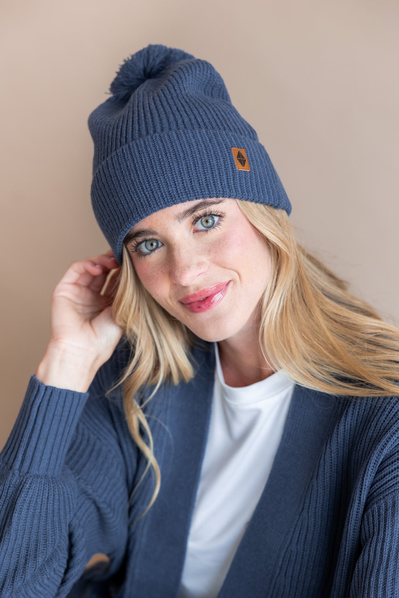 Modal wearing Chunky Knit Adult Pom Beanie in Oxford over white t-shirt and chunky knit women's cardigan in oxford on a beige background