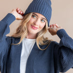 Modal wearing Chunky Knit Adult Ribbed Beanie in oxford over white t-shirt and chunky knit women's cardigan in oxford on a beige background