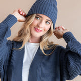 Modal wearing Chunky Knit Adult Ribbed Beanie in oxford over white t-shirt and chunky knit women's cardigan in oxford on a beige background