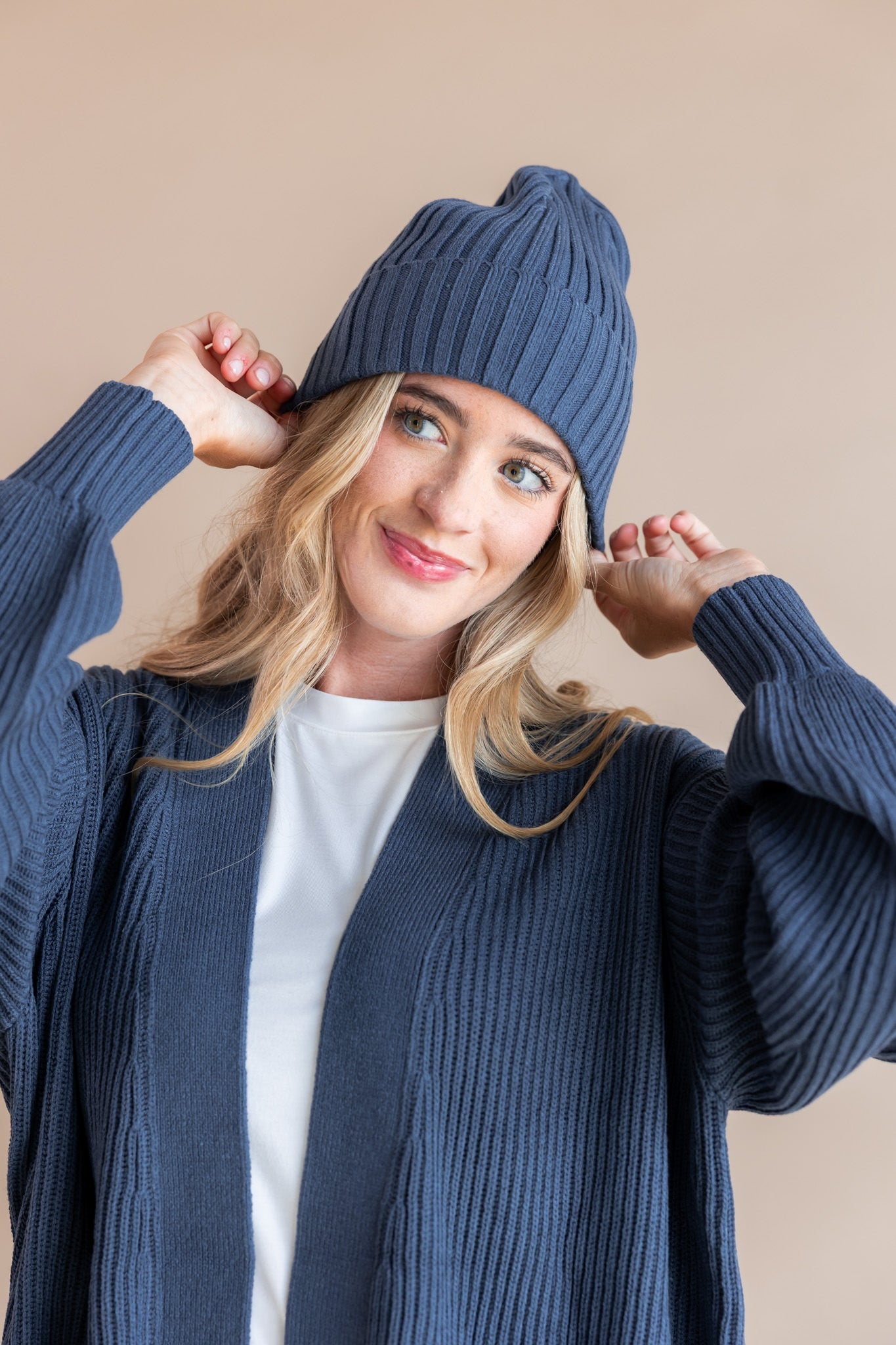 Modal wearing Chunky Knit Adult Ribbed Beanie in oxford over white t-shirt and chunky knit women's cardigan in oxford on a beige background
