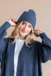 Modal wearing Chunky Knit Adult Ribbed Beanie in oxford over white t-shirt and chunky knit women's cardigan in oxford on a beige background