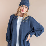 Modal wearing Chunky Knit Adult Ribbed Beanie in oxford over white t-shirt and chunky knit women's cardigan in oxford and blue jeans on a beige background