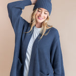 Modal wearing Chunky Knit Adult Ribbed Beanie in oxford over white t-shirt and chunky knit women's cardigan in oxford on a beige background