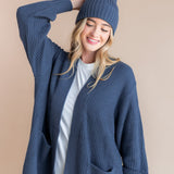 Modal wearing Chunky Knit Adult Ribbed Beanie in oxford over white t-shirt and chunky knit women's cardigan in oxford on a beige background