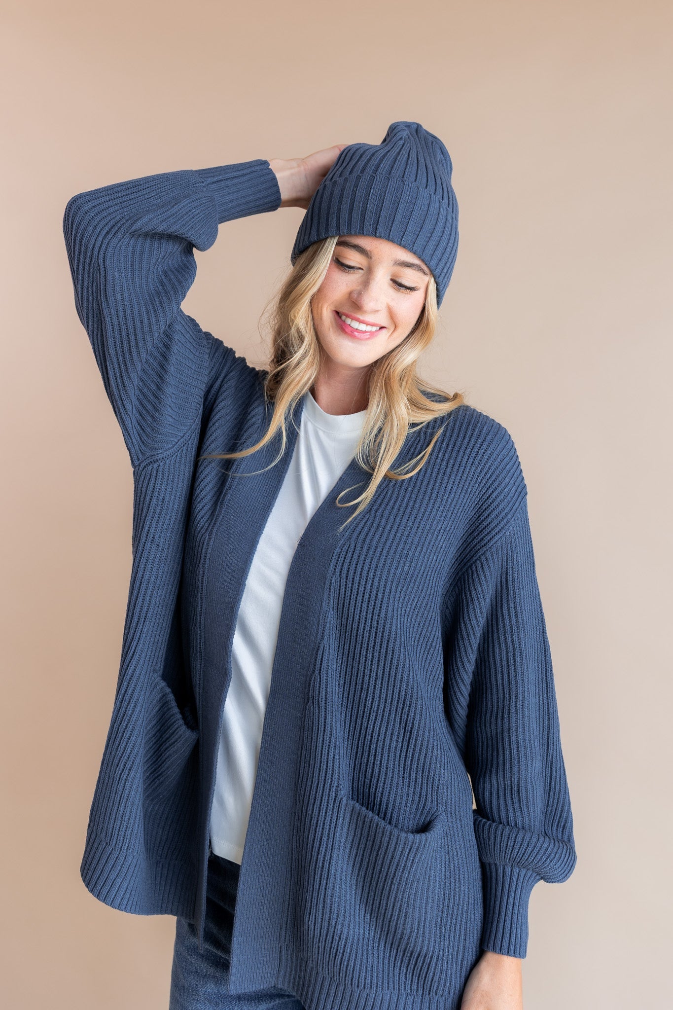 Modal wearing Chunky Knit Adult Ribbed Beanie in oxford over white t-shirt and chunky knit women's cardigan in oxford on a beige background