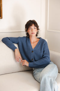 Woman sitting on the couch with her arm propped up in a cropped cardigan in oxford