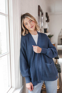 Woman leaning up against the wall wearing an oversized cardigan in oxford
