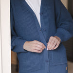 Close up of Modal standing against a wall wearing Chunky Knit Women's Waffle Cardigan in Oxford with buttons over white t-shirt and blue jeans