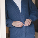 Close up of Modal standing against a wall wearing Chunky Knit Women's Waffle Cardigan in Oxford with buttons over white t-shirt and blue jeans