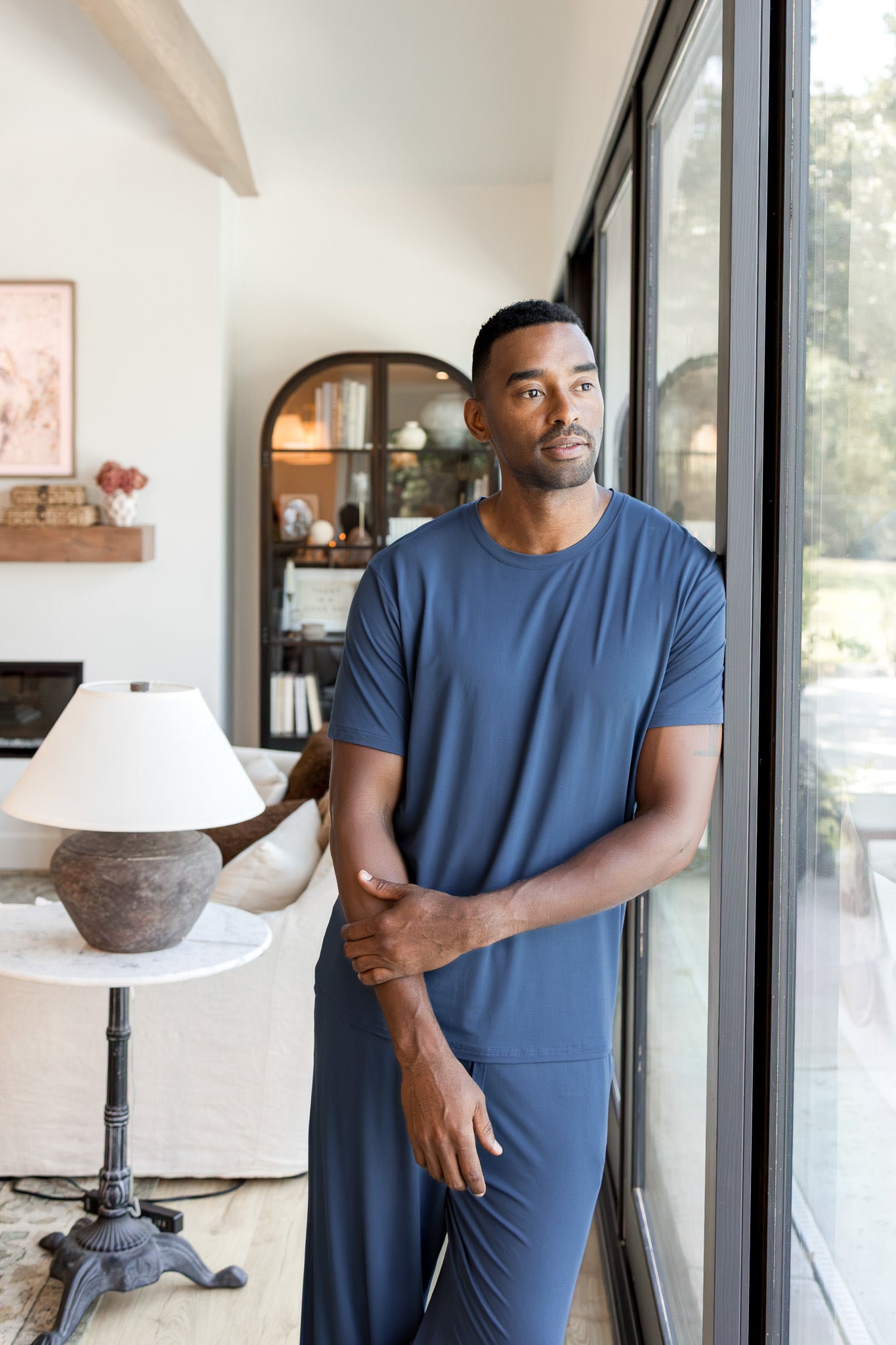 Male model wearing a oxford blue crew neck tee and matching pant in a living room