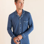 Male model wearing oxford blue button up long sleeve pajamas in a studio setting, holding cuff
