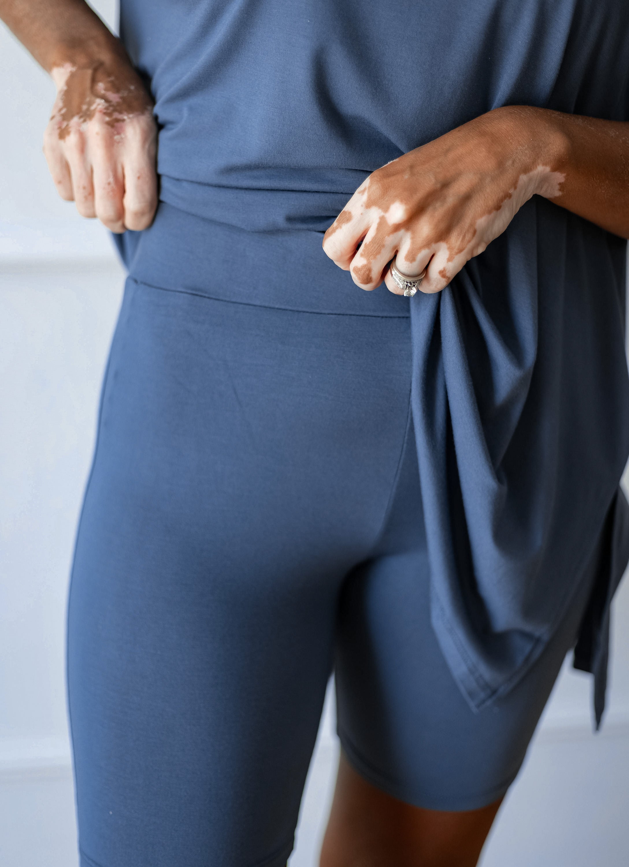 Close-up of a person wearing slate blue athletic shorts and a matching top, with hands adjusting the waist area. 