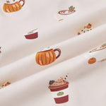 A repeating, all-over print featuring: a white cappuccino cup with latte art and a green leaf garnish, next to a mini pumpkin and a dusting of cocoa powder; an orange pumpkin-shaped mug with whipped cream and garnished with star anise and a cinnamon stick; a rust-colored to-go coffee cup with orange whipped cream, a dark green leaf, and a straw; and a yellow mug with a maple leaf image, topped with whipped cream, cloves, and a mini orange pumpkin, over a light beige background color named Vanilla.
---1605 1