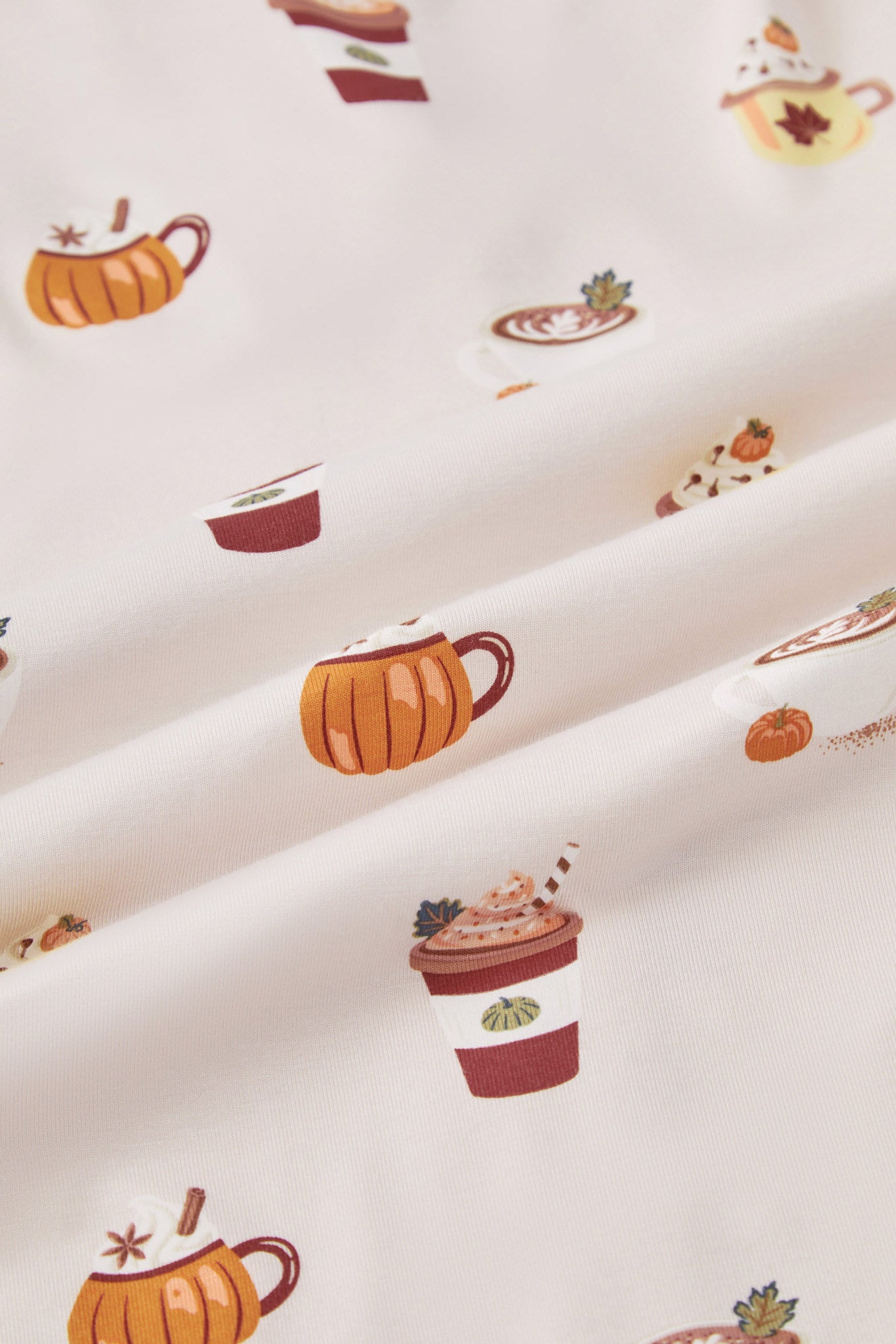 A repeating, all-over print featuring: a white cappuccino cup with latte art and a green leaf garnish, next to a mini pumpkin and a dusting of cocoa powder; an orange pumpkin-shaped mug with whipped cream and garnished with star anise and a cinnamon stick; a rust-colored to-go coffee cup with orange whipped cream, a dark green leaf, and a straw; and a yellow mug with a maple leaf image, topped with whipped cream, cloves, and a mini orange pumpkin, over a light beige background color named Vanilla.
---1605 1